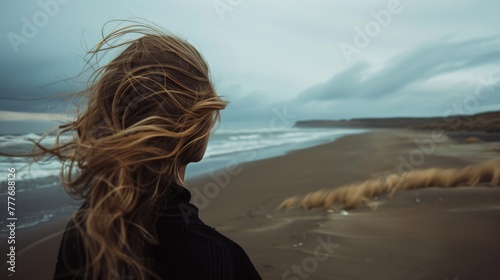 Wind-swept woman on a deserted beach at dusk. Dramatic landscape portrait with dynamic hair movement. © AIS Studio