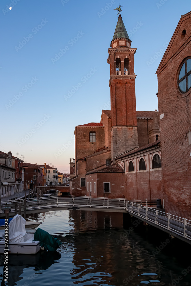 Church of Saint James Apostle with view of canal Vena nestled in charming town of Chioggia, Venetian Lagoon, Veneto, Italy. Small boats floating in calm water creating romantic reflections. Tourism