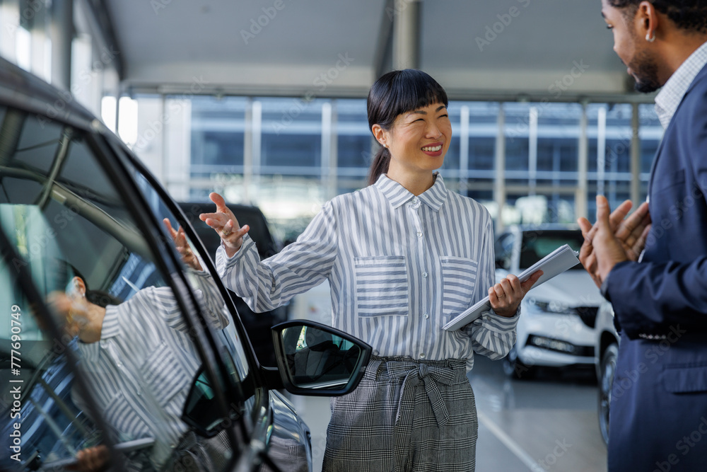 Asian sales manager showing new car to customer Asian sales manager showing new car to customer