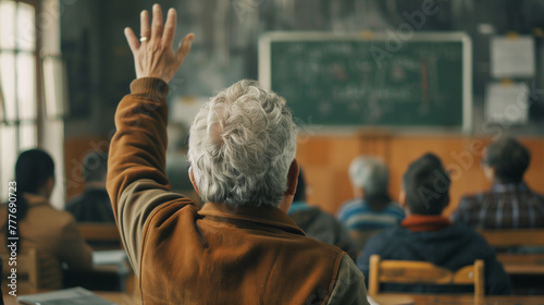 Back view of older student raising his hand to answer teacher's question during education training class
