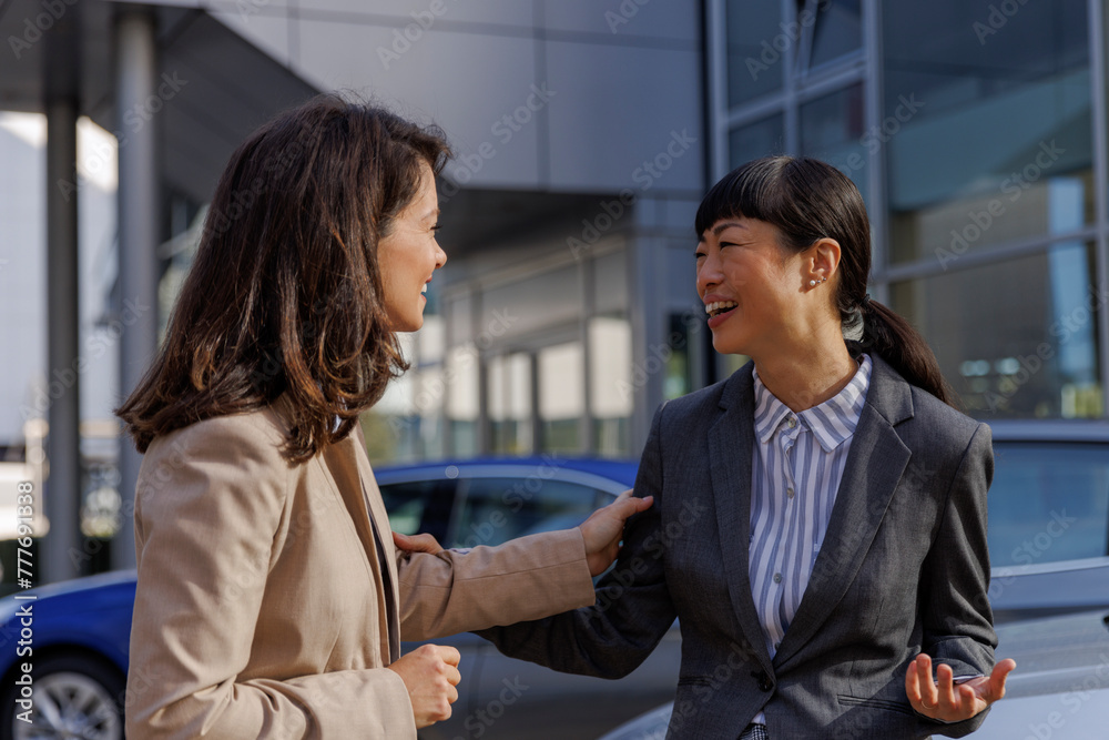 Female colleagues talking while working at car dealership Female colleagues talking while working at car dealership