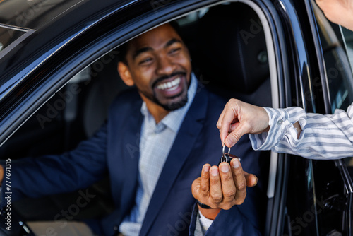 Happy man taking new car keys from sales executive at dealership photo