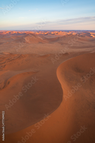 Breathtaking sunrise over the sand dunes of Sossusvlei, Namibia, captured from a helicopter. The first light of dawn casts dramatic shadows and highlights the vibrant colors of the desert.
