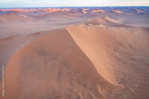 Breathtaking sunrise over the sand dunes of Sossusvlei, Namibia, captured from a helicopter. The first light of dawn casts dramatic shadows and highlights the vibrant colors of the desert.
