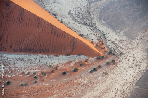 Breathtaking sunrise over the sand dunes of Sossusvlei, Namibia, captured from a helicopter. The first light of dawn casts dramatic shadows and highlights the vibrant colors of the desert.