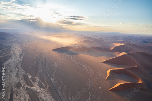 Breathtaking sunrise over the sand dunes of Sossusvlei, Namibia, captured from a helicopter. The first light of dawn casts dramatic shadows and highlights the vibrant colors of the desert.
