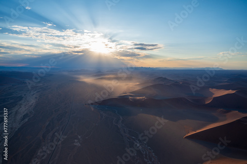 Breathtaking sunrise over the sand dunes of Sossusvlei, Namibia, captured from a helicopter. The first light of dawn casts dramatic shadows and highlights the vibrant colors of the desert.