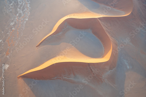 Breathtaking sunrise over the sand dunes of Sossusvlei, Namibia, captured from a helicopter. The first light of dawn casts dramatic shadows and highlights the vibrant colors of the desert.
