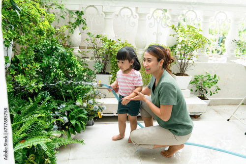 Happy young mother and daughter watering plants