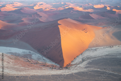Breathtaking sunrise over the sand dunes of Sossusvlei, Namibia, captured from a helicopter. The first light of dawn casts dramatic shadows and highlights the vibrant colors of the desert.