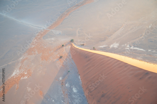 Breathtaking sunrise over the sand dunes of Sossusvlei, Namibia, captured from a helicopter. The first light of dawn casts dramatic shadows and highlights the vibrant colors of the desert.