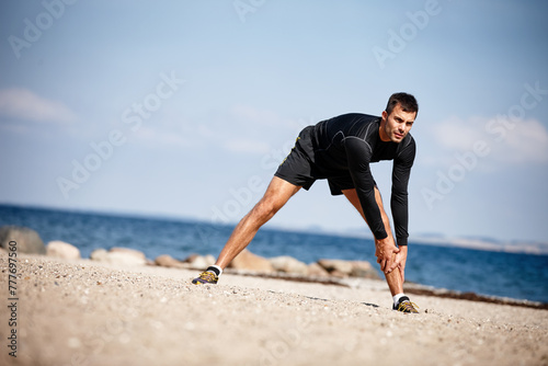 Man, stretching and sports at beach for exercise with fitness motivation, sand and blue sky. Male person, training and nature by ocean with workout for wellness, strong body and health activity