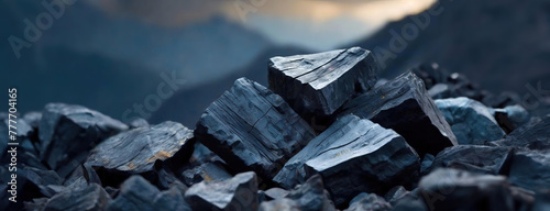 Coal pieces pile up, hinting at fossil fuels and energy. The carbon rich deposits sit against a dim twilight, alluding to mining and power. Panorama with copy space.