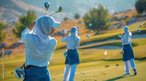 Three women Muslim in hijab are playing golf, one of them is wearing a blue skirt. The women are standing on a green field and are holding golf clubs