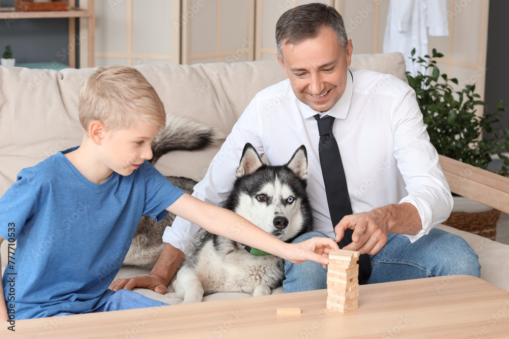 Mature doctor with his little son and cute dog playing game on sofa at home