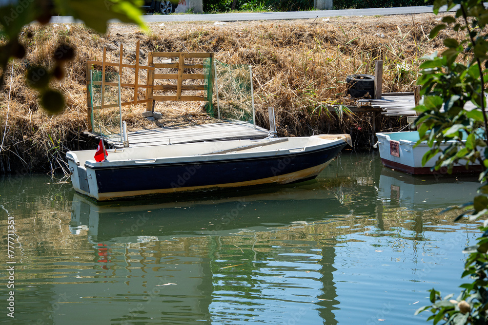 Obraz premium Old wooden fishing boats on a calm river. Boat moored in a canal on a sunny summer day. Fishing boats on the river in autumn
