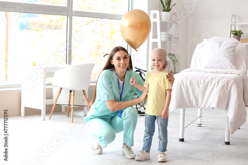 Little girl after chemotherapy with golden balloon and nurse in clinic photo
