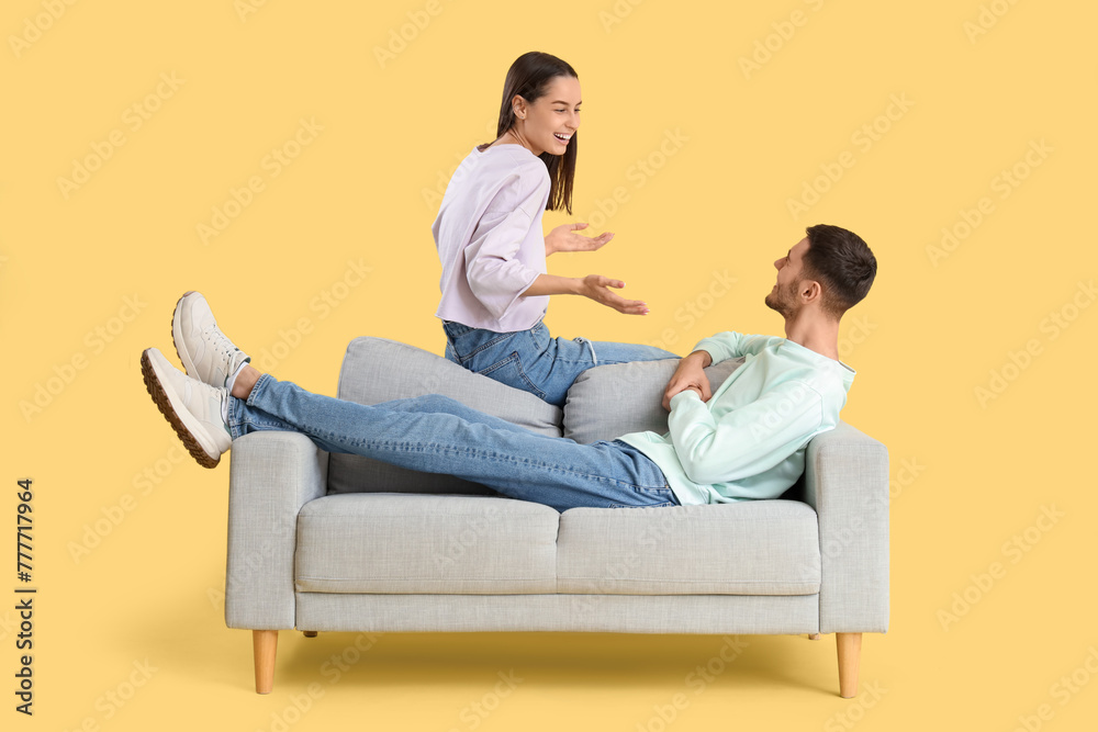 Beautiful young happy couple spending time together on sofa against yellow background Beautiful young happy couple spending time together on sofa against yellow background