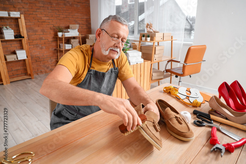 Mature shoemaker brushing shoe at table in workshop