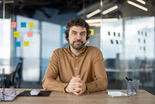 Professional man in a brown shirt wearing a headset, sitting confidently at his workplace in a modern office.