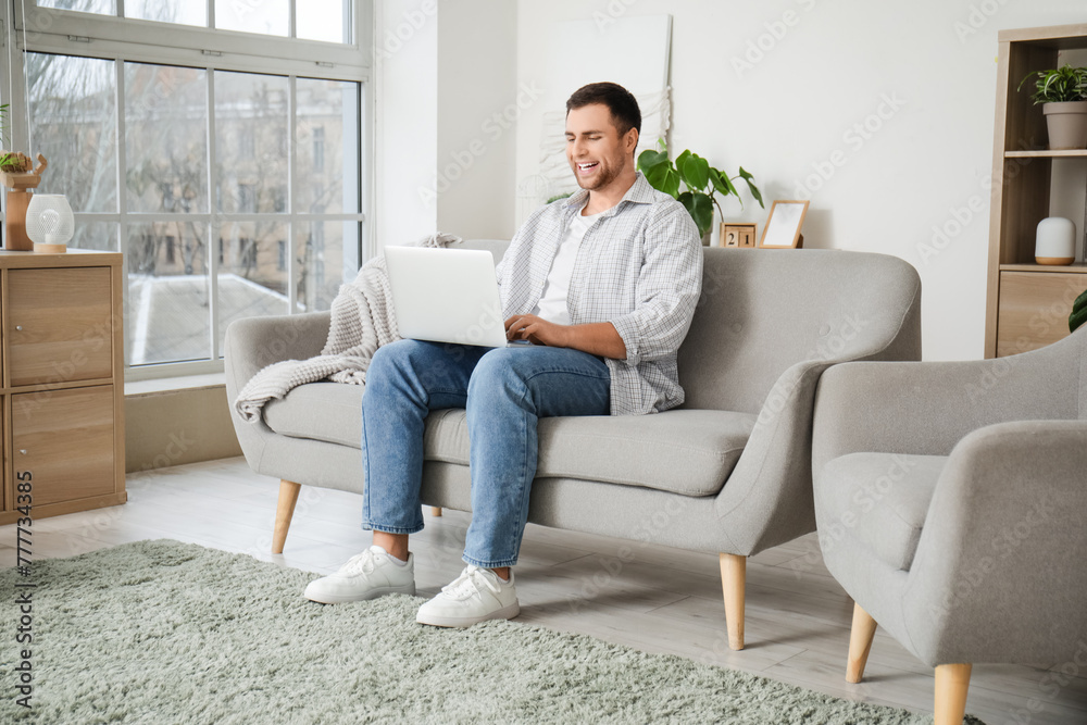 Young man using laptop on grey sofa at home Young man using laptop on grey sofa at home