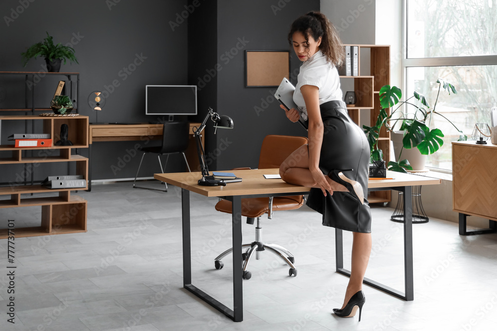 Attractive African-American secretary with laptop near table in office Attractive African-American secretary with laptop near table in office