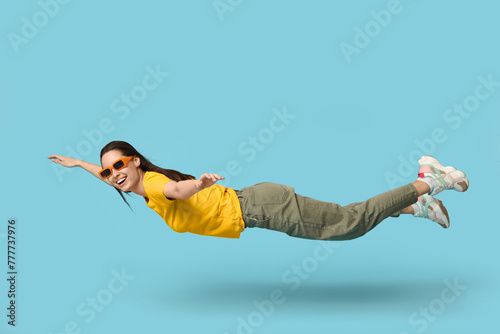 Joyful young woman in sunglasses flying on blue background