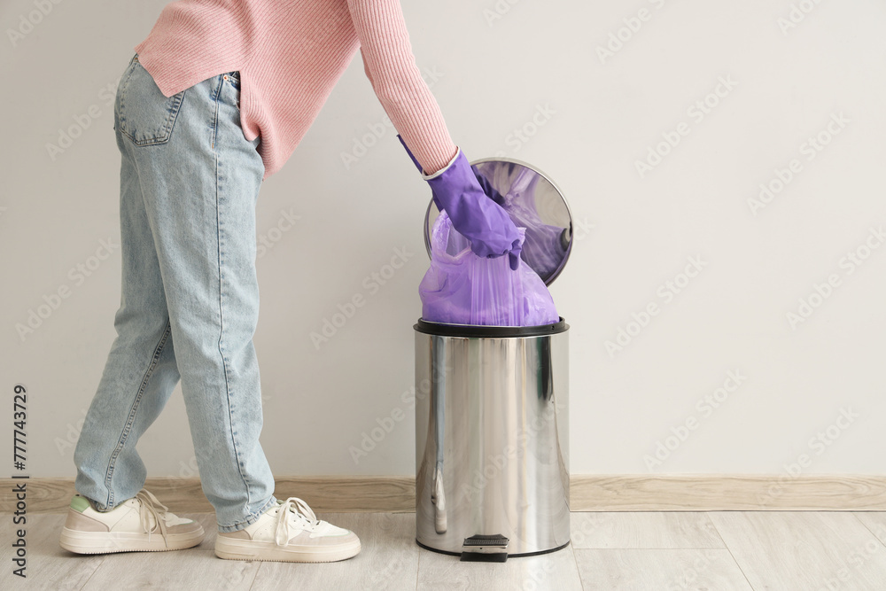 Woman taking garbage bag from trash bin near white wall Woman taking garbage bag from trash bin near white wall