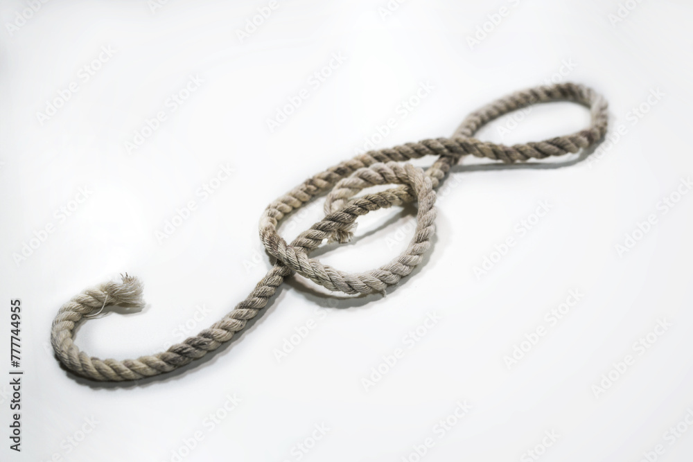 Old rough rope laying in the shape of a treble clef or violin key on a light gray background, musical symbol, copy space, selected focus