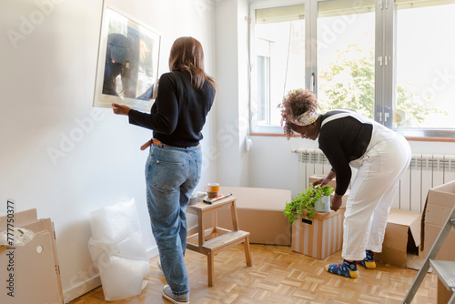 Women decorating and unpacking boxes in new home while moving in photo