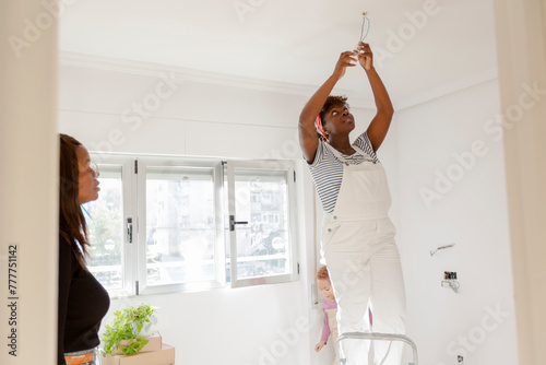 Pregnant woman on ladder changing bulb in new home photo