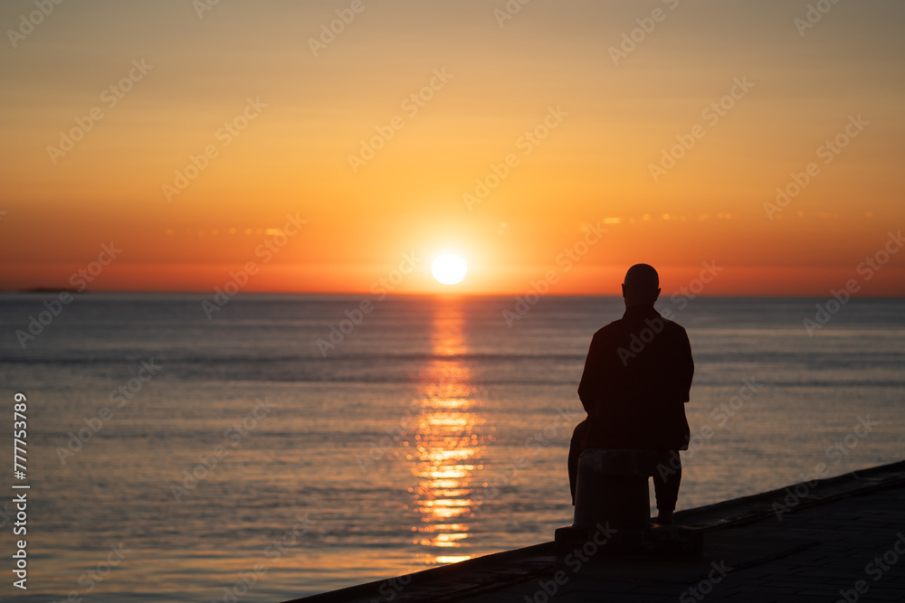 A man sitting watching the sunset at the ocean