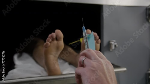 Doctor with embalming syringe in front of a morgue body photo