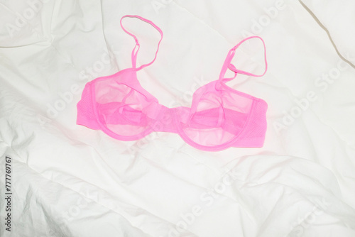 Hot pink transparent mesh bra / lingerie laying on bed with bedsheets photo