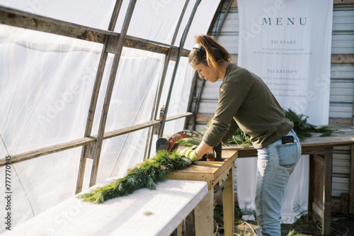 female farmer working with machine to tie pine garland in greenhouse photo