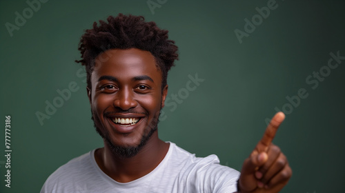 A handsome man with a big smile showing teeth, pointing his finger at an empty space, with a green background. 