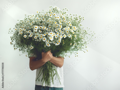 Young man hiding behind a large bouquet of wild daisy flowers, on white background. Flowers from the garden for birthday, anniversary, midsummer celebration. Copy space.