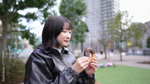 Slow motion video of a Japanese woman in her 20s eating donuts in a park around Gotanda Station in Shinagawa-ku, Tokyo in winter 冬の東京都品川区五反田の駅周辺の公園でドーナツを食べる20代の日本人女性のスローモーション映像 photo