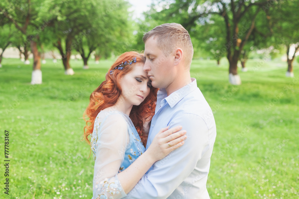 young couple in love hugging. woman with fiery hair in a blue dress. photo shoot in an apple orchard