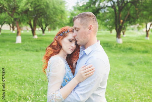 young couple in love hugging. woman with fiery hair in a blue dress. photo shoot in an apple orchard