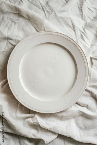 An empty white plate on a crumpled grey fabric background