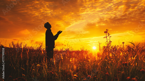 Silhouette of a man praying in the meadow at sunset