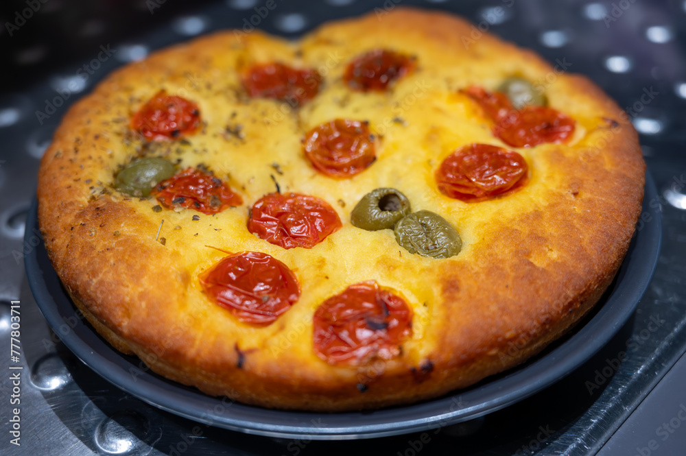 Tasty italian vegetarian food, fresh baked flat foccachia bread with cherry tomatoes, olives and herbs close up