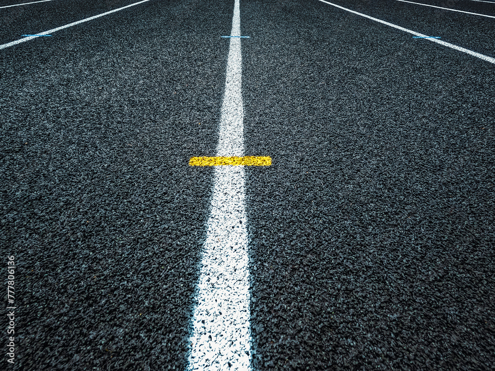 Track and Field Running Lanes. Overhead view of a rubber black running track surface with white lane lines. Yellow dash line at the center of view. Overhead view of the textured rubber black surface. Track and Field Running Lanes. Overhead view of a rubber black running track surface with white lane lines. Yellow dash line at the center of view. Overhead view of the textured rubber black surface.