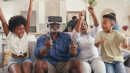 Grandparents with grandchildren wearing virtual reality headset -playing game at home together - shot in slow motion photo