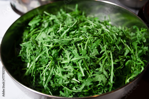 Fresh Arugula Leaves in a Stainless Steel Bowl. A bowl full of vibrant green arugula leaves, freshly washed and ready for salad preparation.