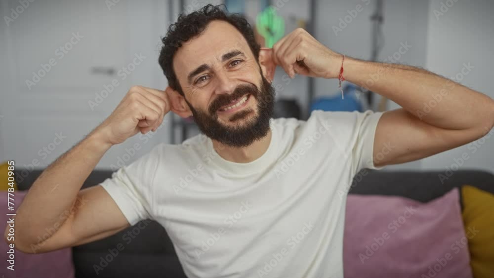Cheerful middle-aged hispanic man making funny face, pulling ears with fingers in a white t shirt at home, audition problem or just comical relief? Cheerful middle-aged hispanic man making funny face, pulling ears with fingers in a white t shirt at home, audition problem or just comical relief?