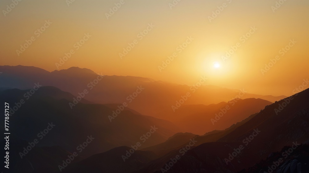 Serene mountain silhouette against the sunset sky - This image captures the tranquil beauty of layered mountain silhouettes basking in the orange glow of a setting sun