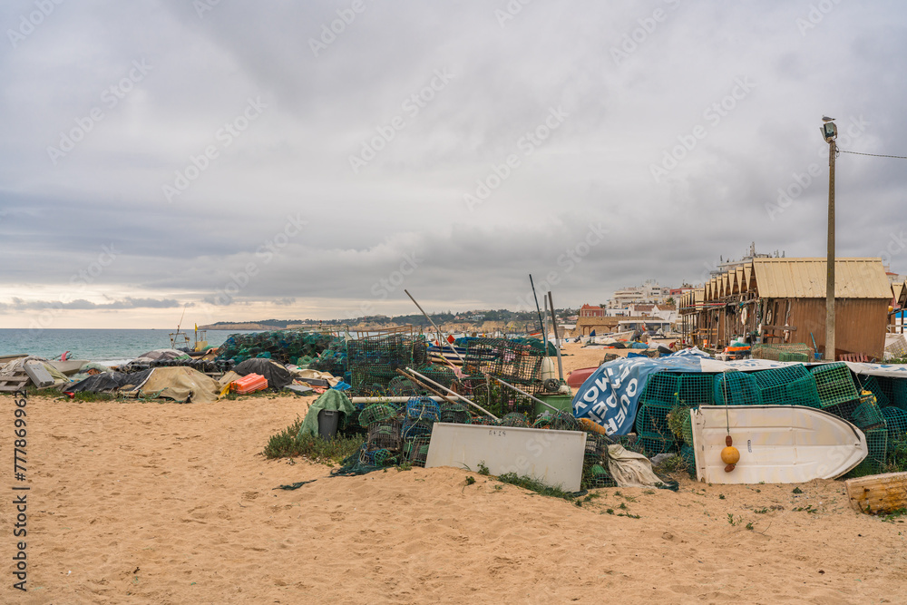 Fishing gear and boats scattered on a sandy beach under a cloudy sky.