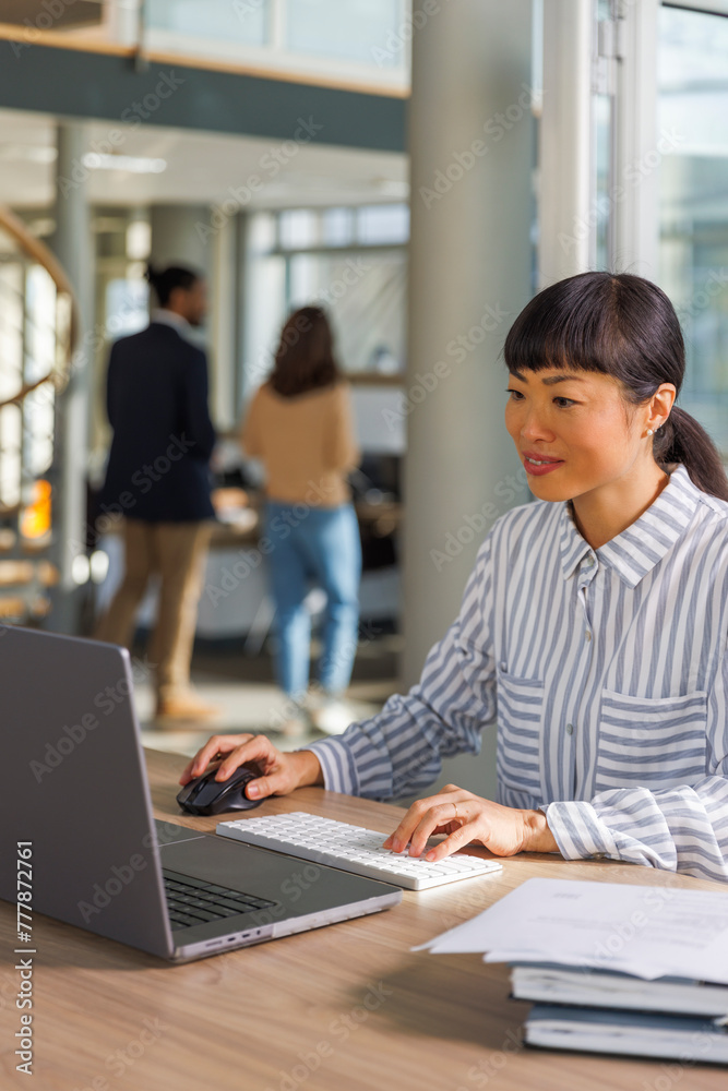 Professional working on laptop with colleagues in background Professional working on laptop with colleagues in background